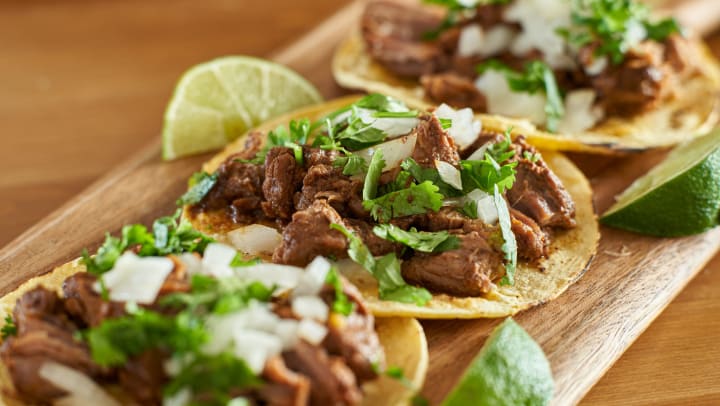 Three Carne Asada tacos with cilantro, onion and lime wedges.