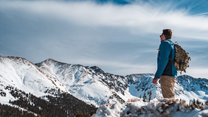 A person with a backpack standing atop a ridge taking in views of snowy mountains