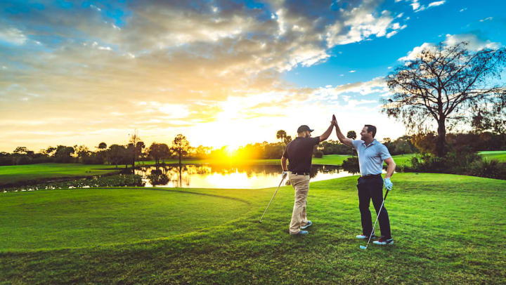 Two men high-fiving on a golf course with the sun setting in the distance