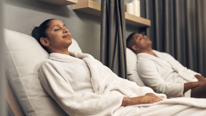 A couple relaxes on reclining chairs while dressed in white robes at a spa