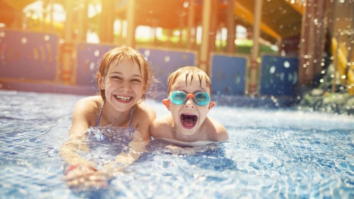 A young girl and boy with huge smiles on their faces. They are laying in a shallow pool at a water park in Destin while they are getting splashed with water.