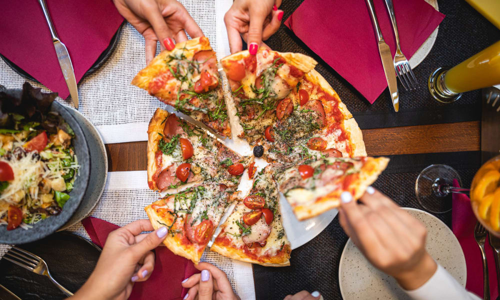 Resident friends diving into a freshly made pizza feast at their favorite restaurant near Pleasanton Place Apartment Homes in Pleasanton, California