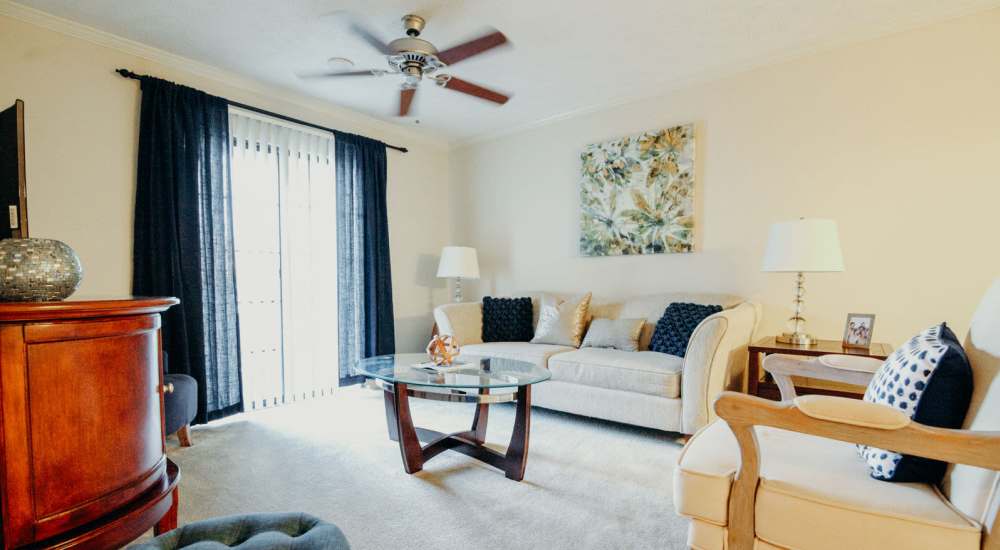 Spacious living room with couch, ceiling fan and glass door leading to balcony at Tapestry on Vaughn in Montgomery, Alabama,  