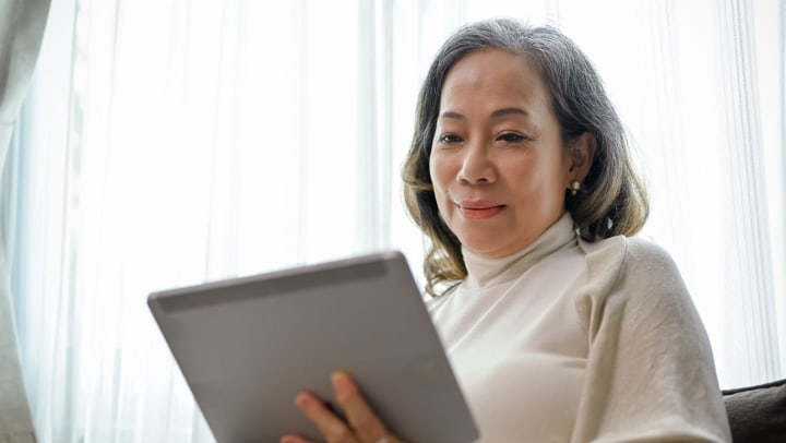 An older woman smiling while holding a tablet