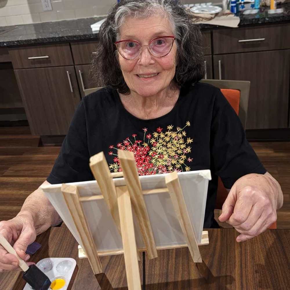 Memory Care resident smiling while painting on a canvas during an art activity at The Landing at Shadow Creek Ranch in Pearland, Texas.