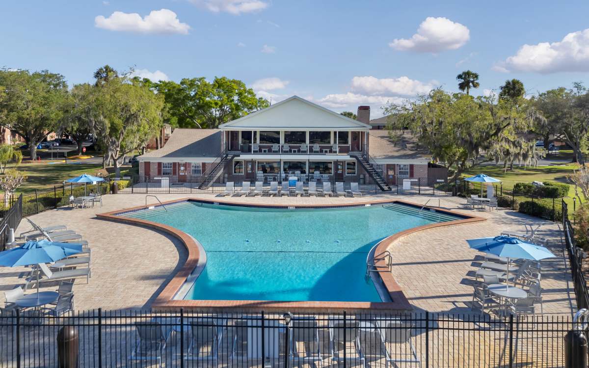 Clean outdoor pool area with lounge seating surrounded by trees at Carlton Arms Of Magnolia Valley in New Port Richey, Florida 