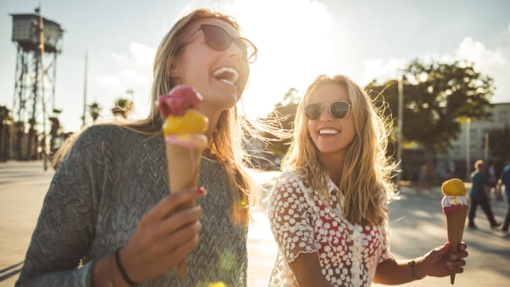 Two smiling women enjoying summer while walking and eating ice cream.