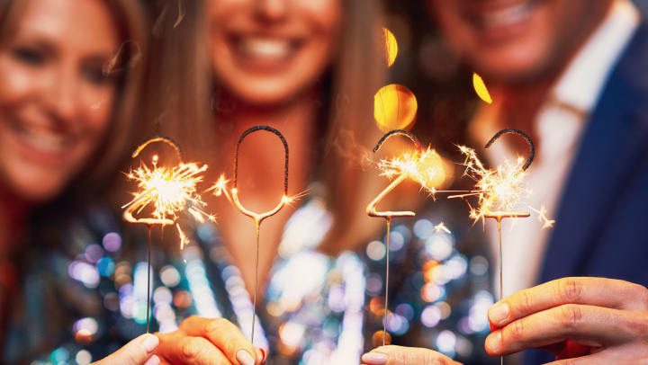 Group of people smiling and holding up sparklers that are in the shape of 2022
