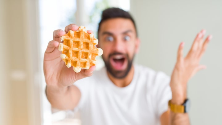 Young man with a surprised face holding a small Belgian waffle