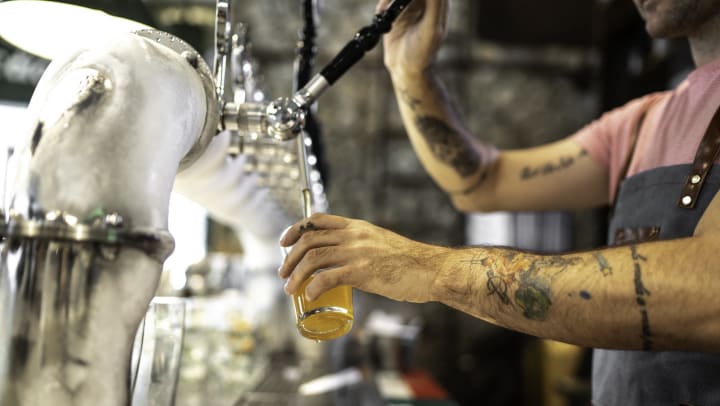 Bartender with tattooed arms pouring beer from a tap