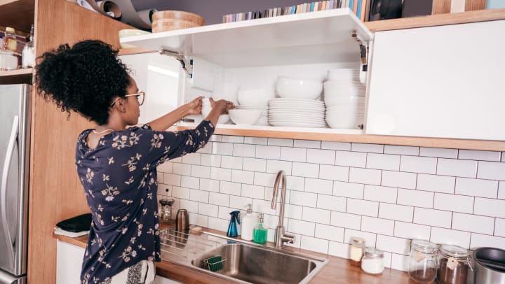 A woman in an upscale apartment putting dishes away in a well-organized kitchen cupboard.