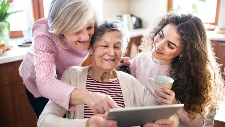A middle-aged woman, elderly woman, and young woman look at a tablet together.