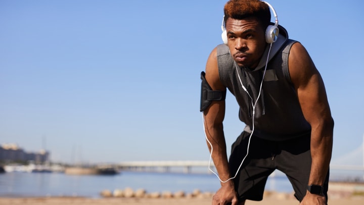 Man resting from hard workout with headphones on and hands on his knees