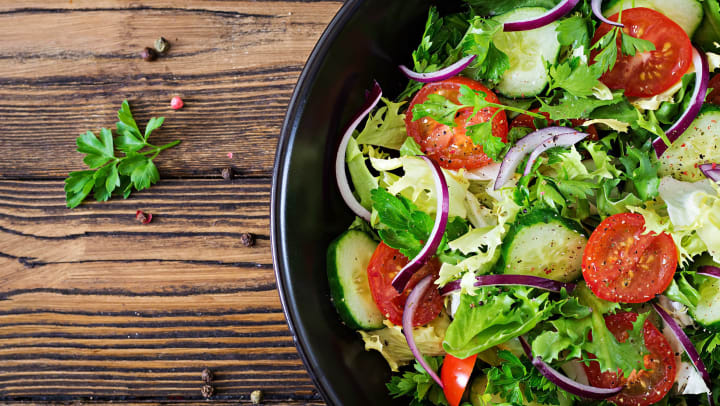 A bowl of fresh greens salad with tomatoes, red onions, and cucumber, seen from above