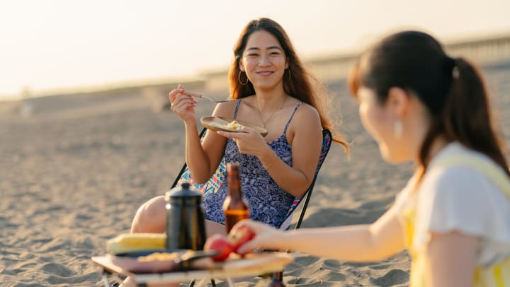Two women sitting on the beach, enjoying a picnic.