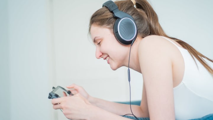 Woman wearing headphones, playing Nintendo Switch in portable mode.