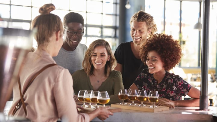 Woman serving beer tasters to a group of people smiling.