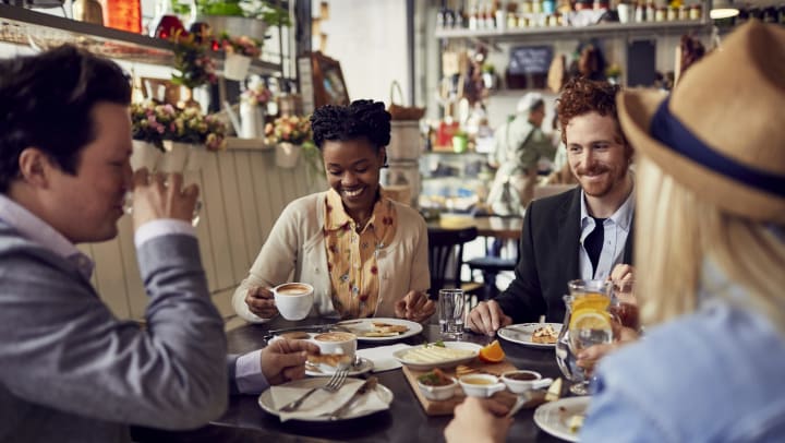 Group of smiling people at a restaurant with coffee and food on the table.