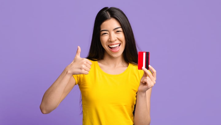 Smiling woman showing thumbs up, holding credit card