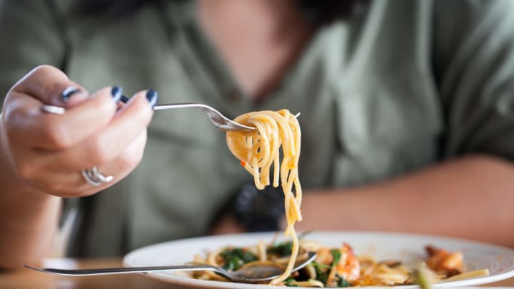 A woman’s hand holding up twirled seafood spaghetti.