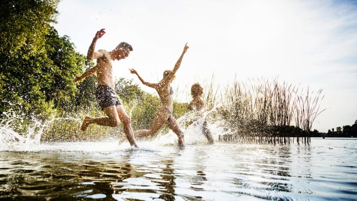 A group of young people in swimsuits running into a stream or lake.
