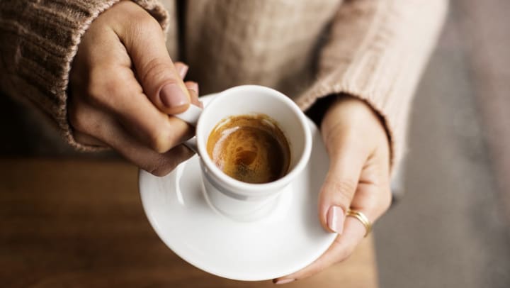 Closeup of hands holding white cup filled with espresso