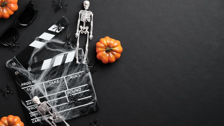 Flat lay composition with clapper board, skeleton, spider web, and pumpkins on a black desk.