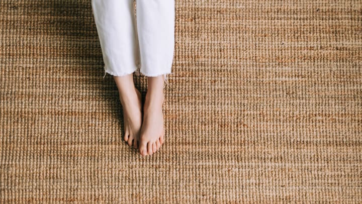 A person wearing white jeans putting their feet on a natural jute rug.