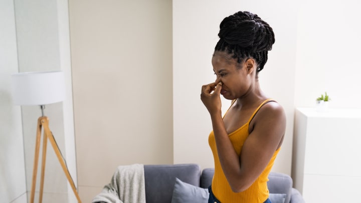 A woman standing in her living room plugging her nose in disgust.