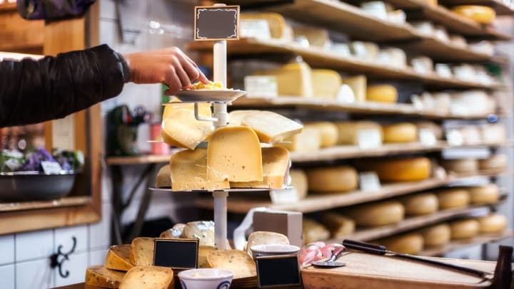 a hand reaches out to taste test some cheese on a multi-tiered display tray on the counter at a cheese shop | cheese shops near Ooltewah