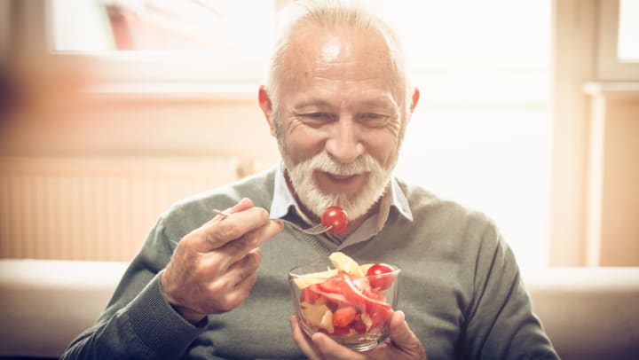 Smiling senior man eating cut tomatoes and vegetables from a glass bowl.