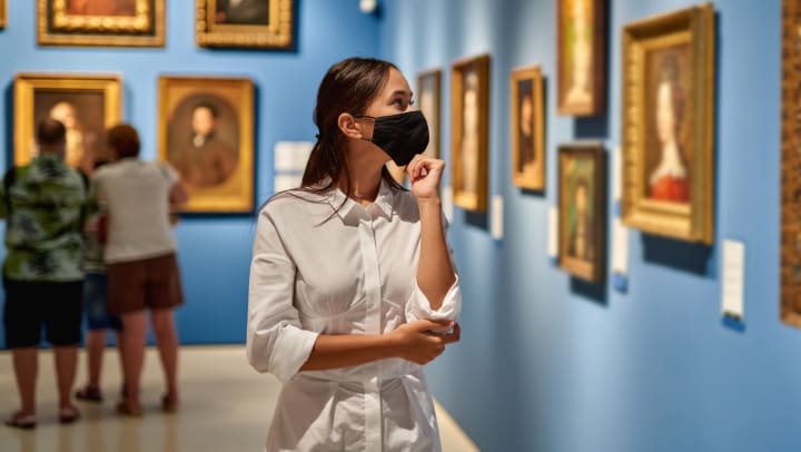 A young woman wearing a mask admiring art in a Meridian museum.