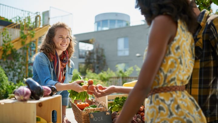 A man and woman purchase produce from a female vendor at a farmers market