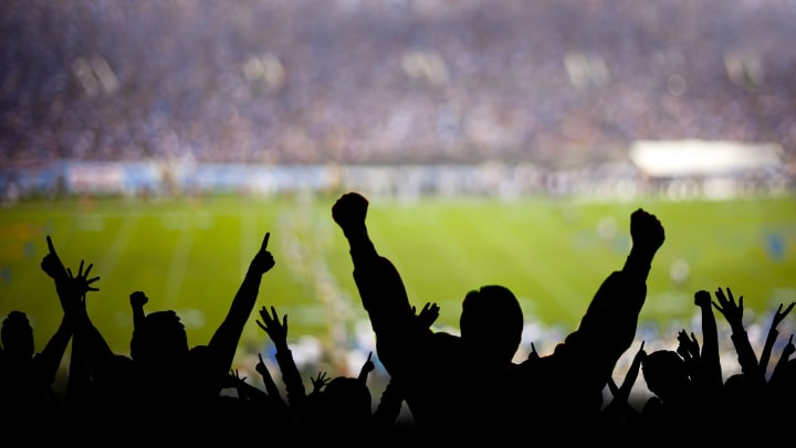A football field in the background. A silhouette of a cheering crowd in the foreground.