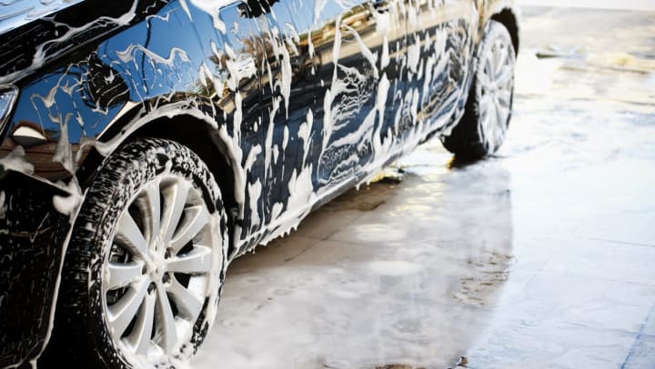A closeup view of a black sedan covered in suds at a car wash in Sarasota.