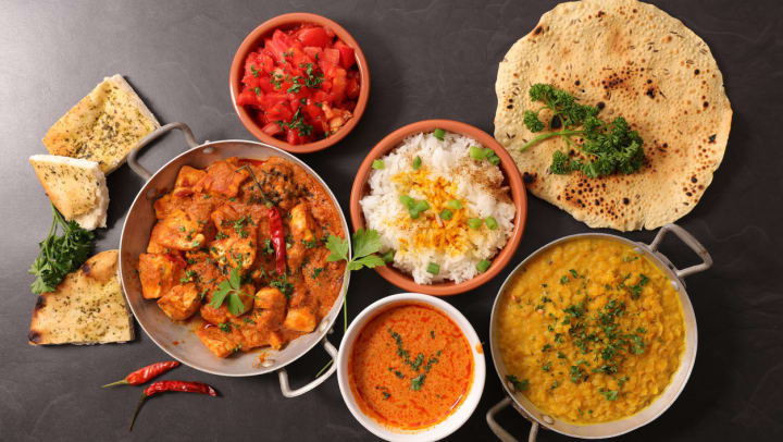 An assortment of Indian food, including naan and dal on a black table