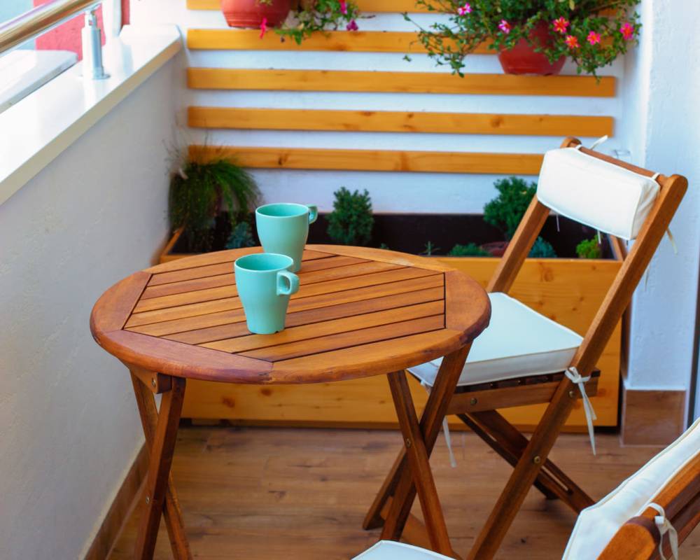 Cozy balcony with wooden table, two teal mugs, and potted plants at ReNew Belcamp in Belcamp, Maryland