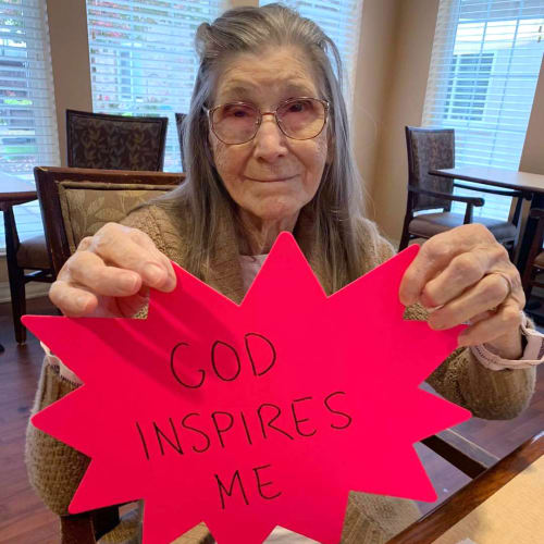 Resident Holding a piece of paper depicting the text 'God inspires me' at Oxford Glen Memory Care at Sachse in Sachse, Texas