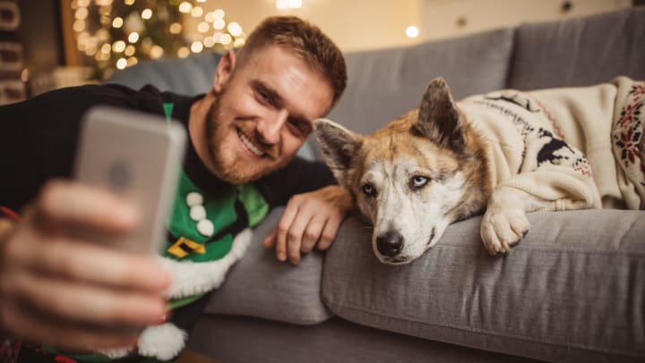 Man wearing ugly Christmas sweater taking a selfie with his dog 