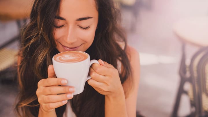 A woman smiling as she drinks a cup of coffee.