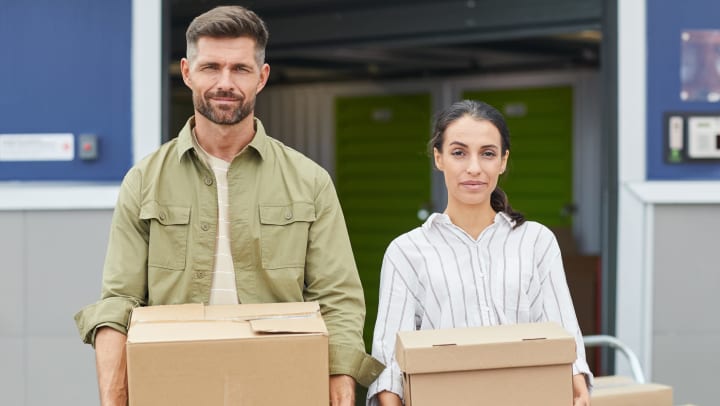 A man and a woman holding boxes in front of an open storage unit.