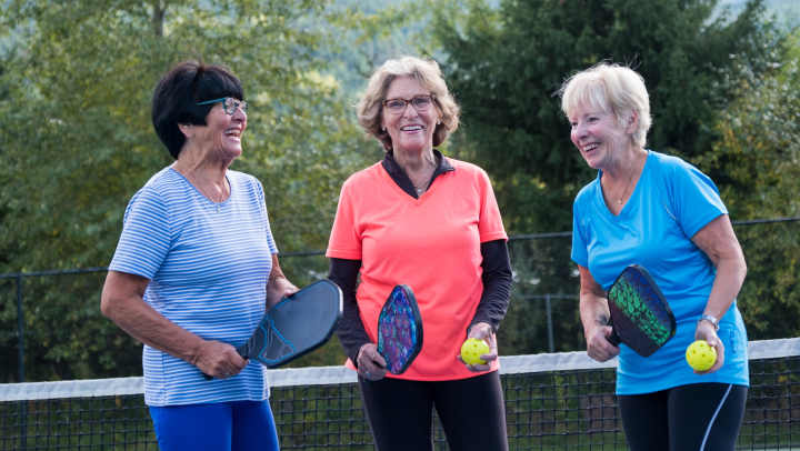Three women smiling and holding Pickle Ball equipment