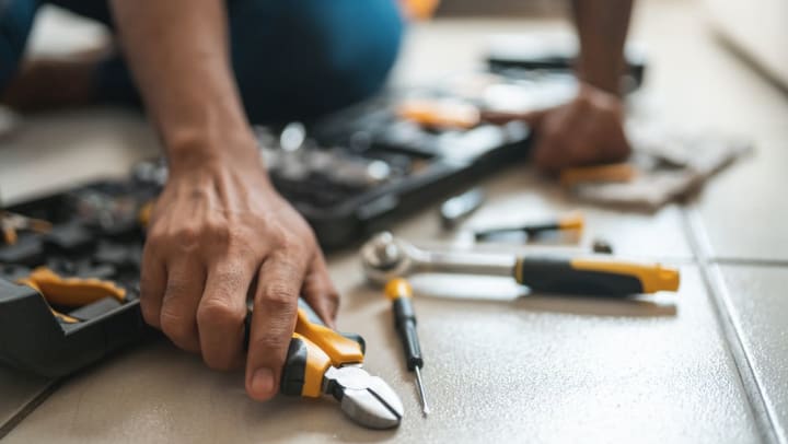 A person sitting on the floor with an open tool box and holding pliers