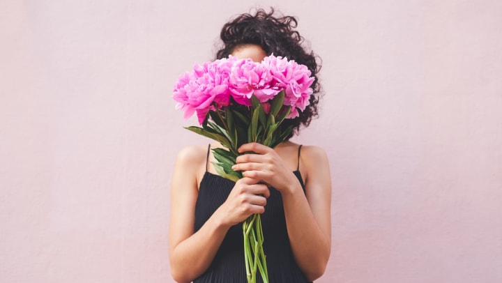 A young woman holds a pink bouquet of flowers in front of her face.