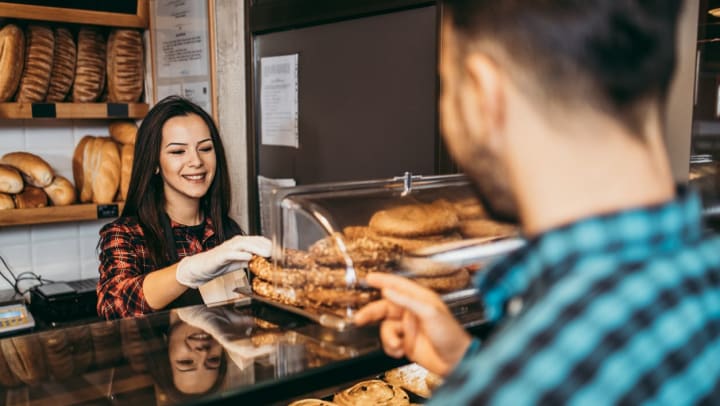 A woman happily giving a pastry to a male customer at a bakery shop in Richmond.