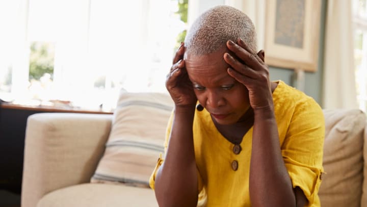 Older woman sitting on couch and holding her head with a blank expression