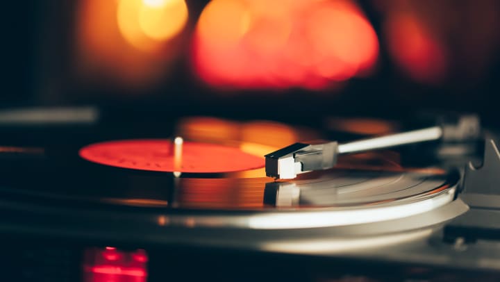 Turntable with LP vinyl record against a fire that is burning in a fireplace in the background
