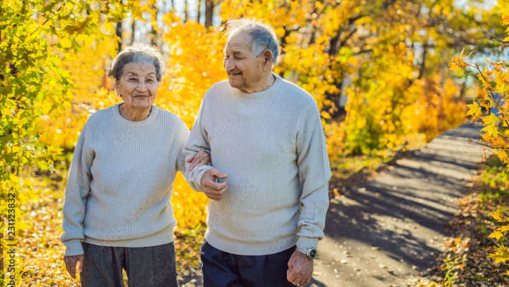 Two seniors standing outside with fall leaves smiling