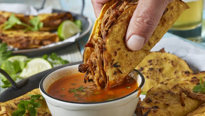 A close-up of a taco being dipped in red salsa | tacos in Keller