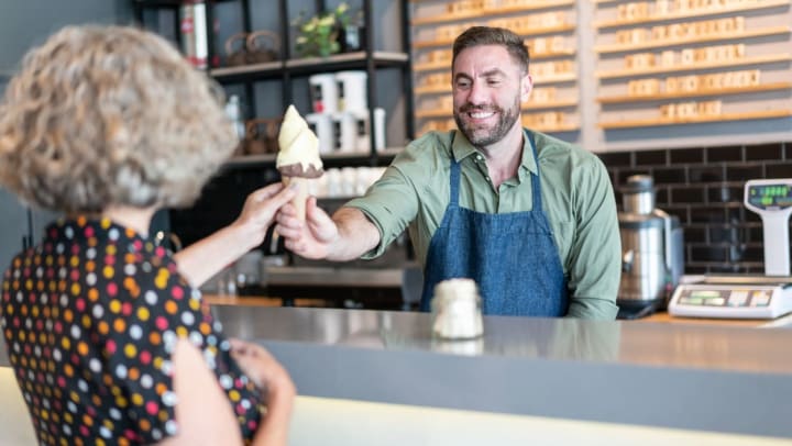 Man behind counter handing over ice cream cone to female customer | ice cream shops in Keller 